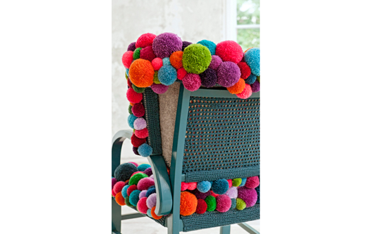 Funda de una silla hecha con pompones de lana de colores